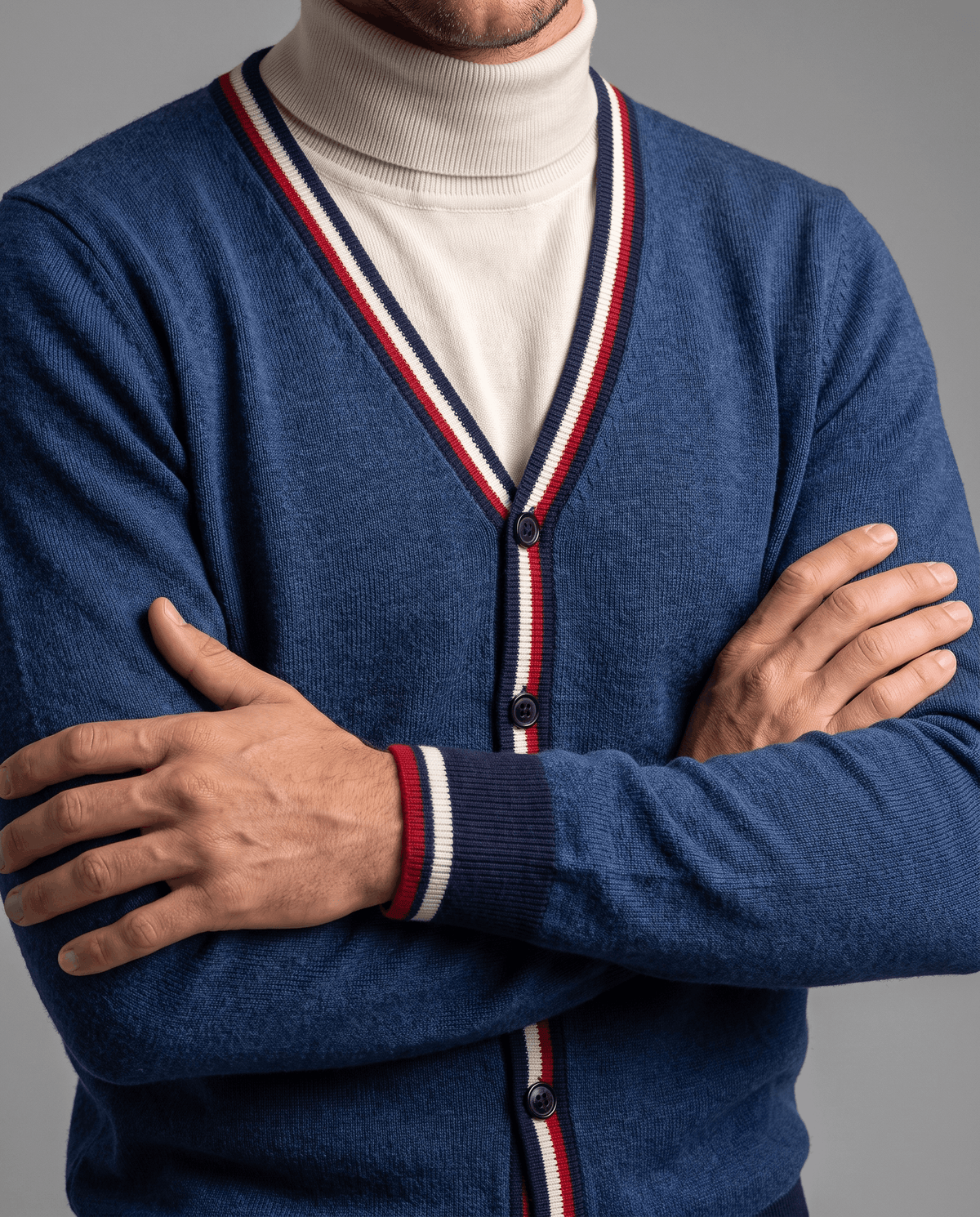 Arms crossed in a blue cardigan over a cream turtleneck showing striped button placket