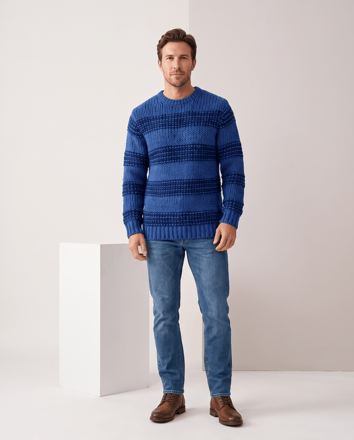 Full-length blue striped crew neck sweater with jeans beside a white wall