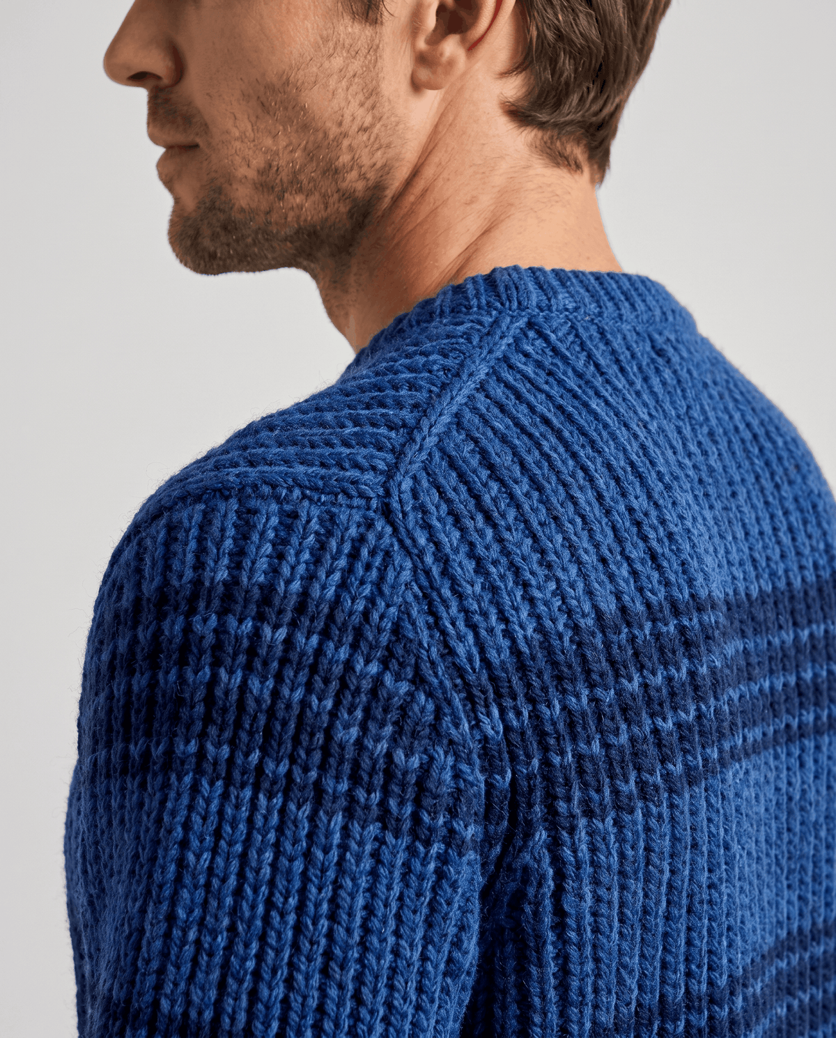 Side close-up of blue sweater shoulder seam and navy stripe detail