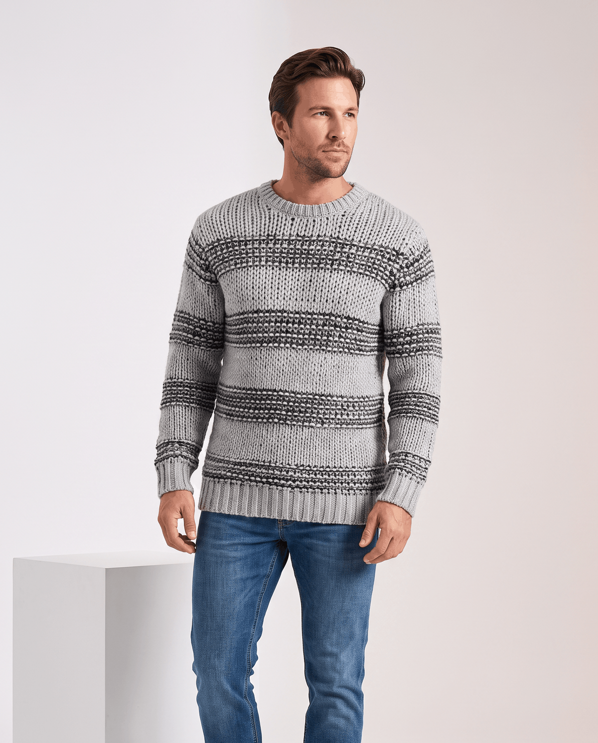 Model in gray striped chunky knit sweater with blue jeans beside a plinth