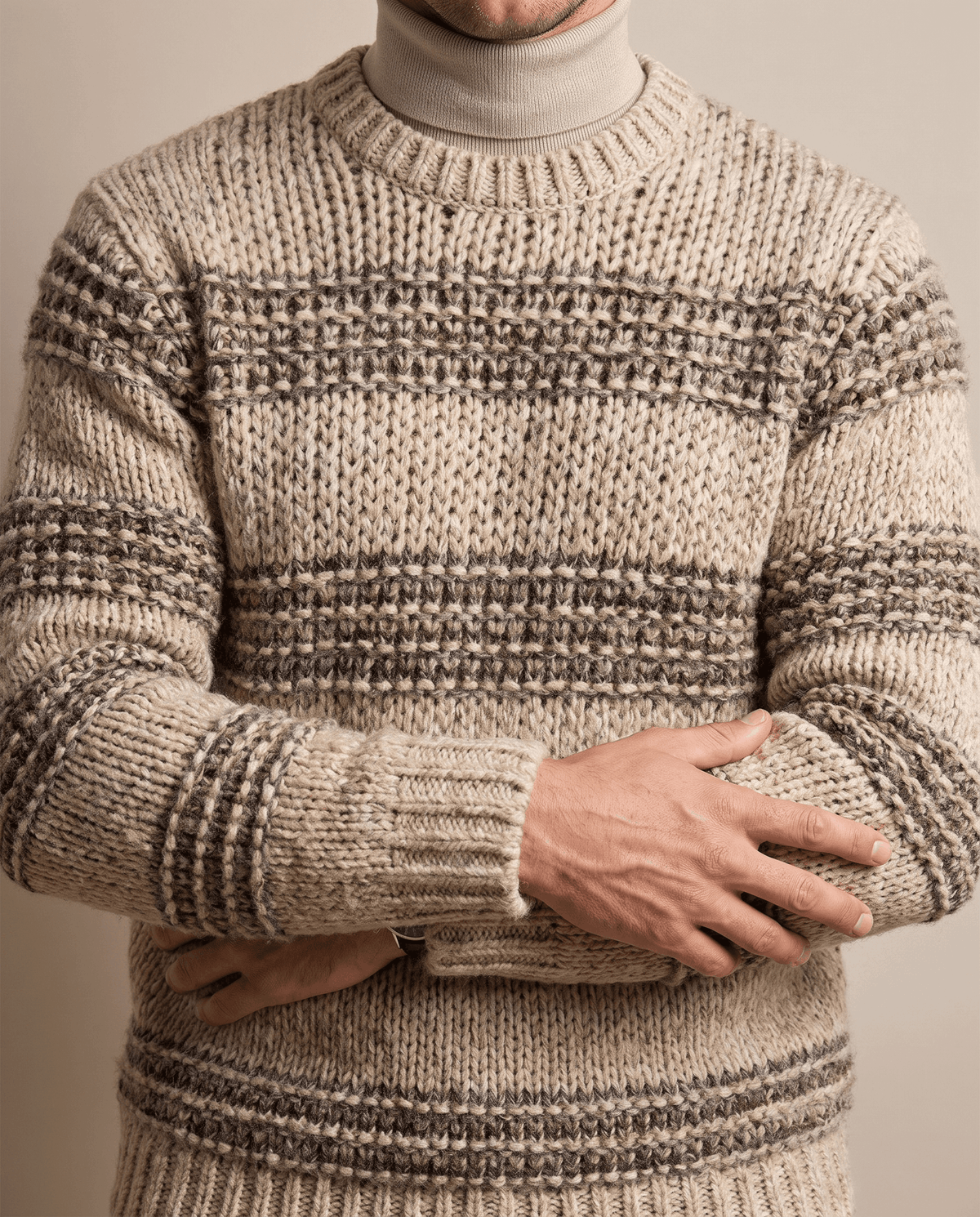 Khaki striped knit worn over beige mock neck with arms folded