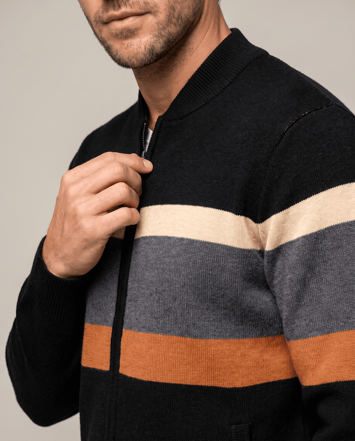 Close-up of hand on the front zip of the black cardigan with cream and orange stripes