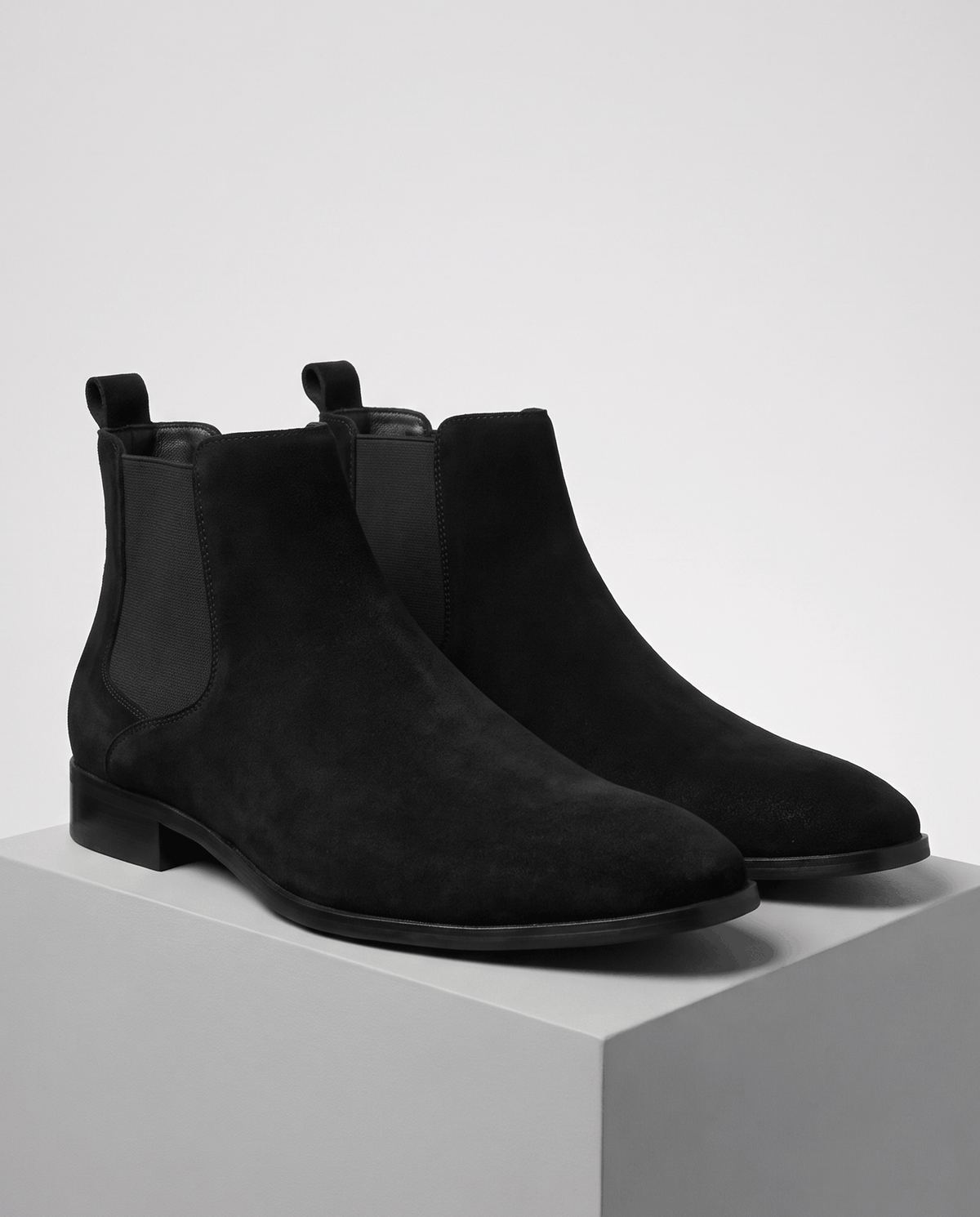 Pair of black suede Chelsea boots on a gray block against a light background