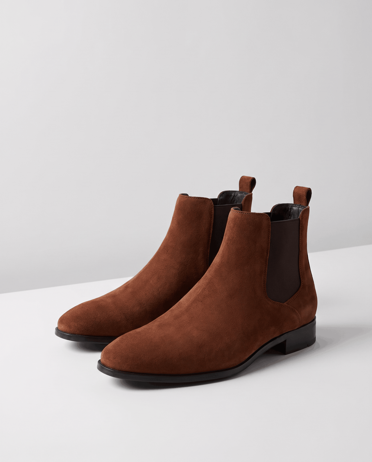 Pair of brown suede Chelsea boots with elastic panels on a white block