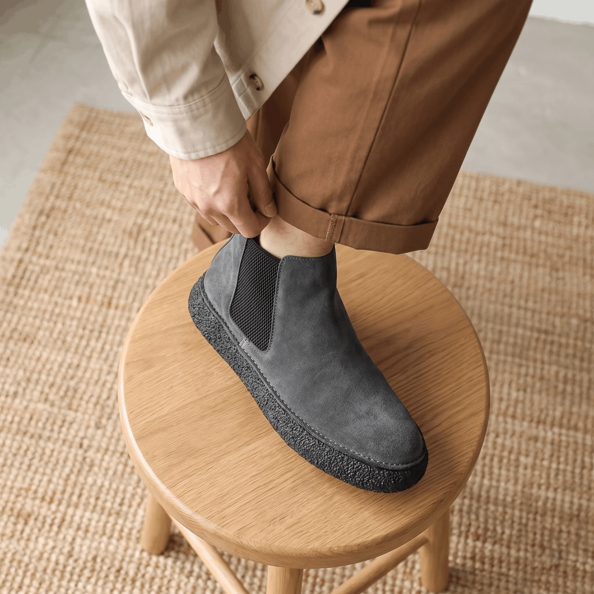 Person wearing gray suede Chelsea boots while standing on a round wooden stool, showing the upper and thick sole.