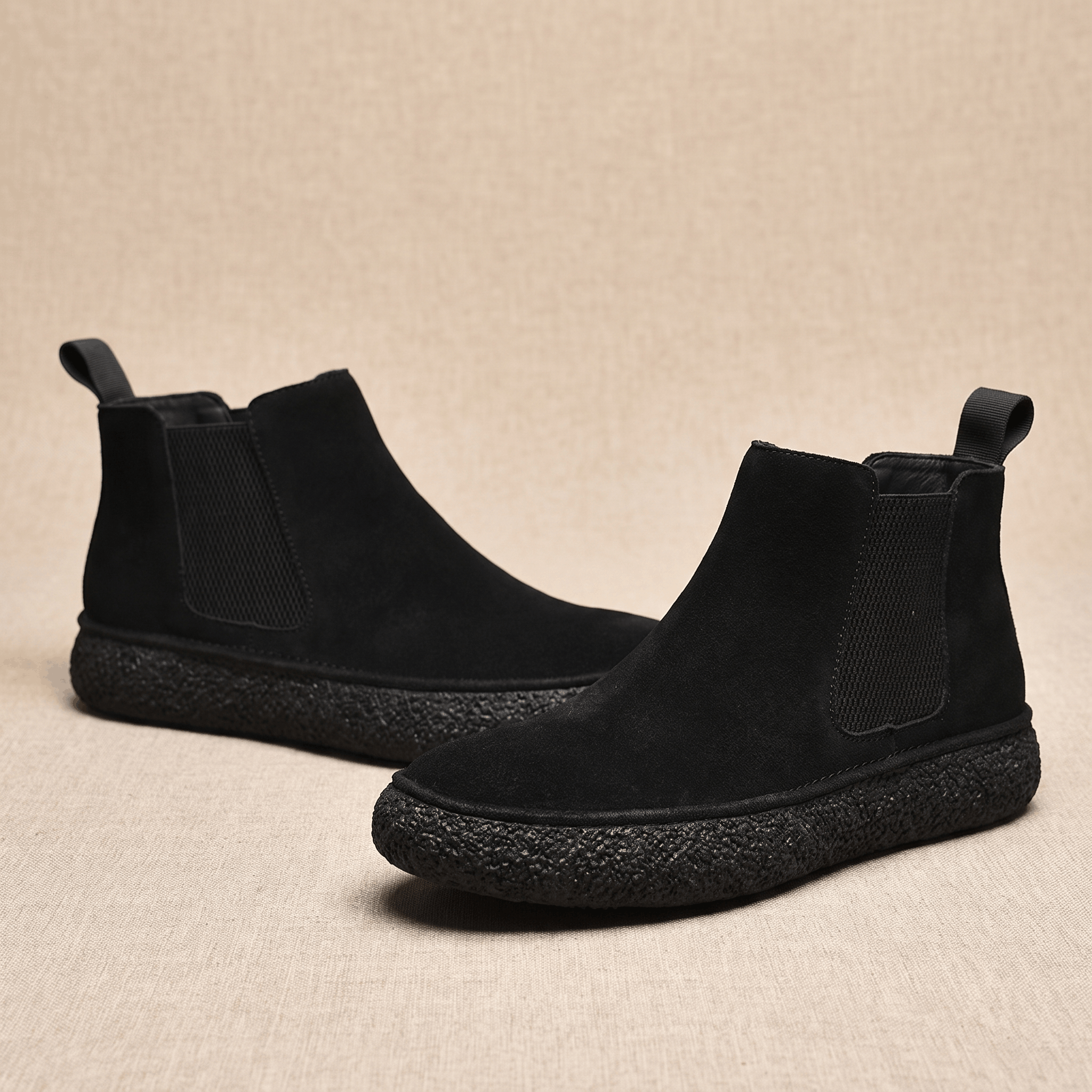Pair of black suede Chelsea boots with elastic side panels, pull tabs, and thick crepe soles on a neutral background.