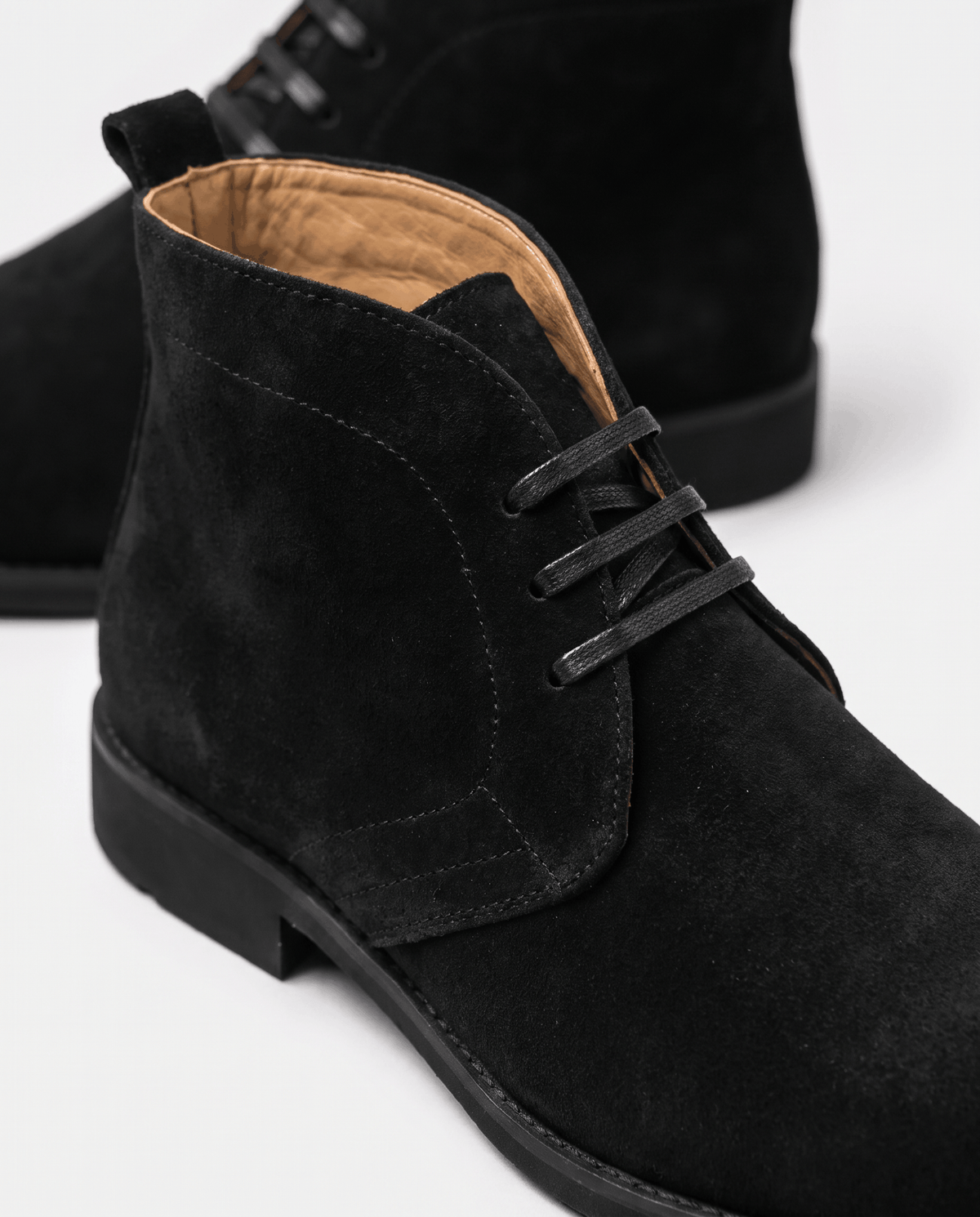 Close-up of black suede chukka boot with short lace-up and tan lining.