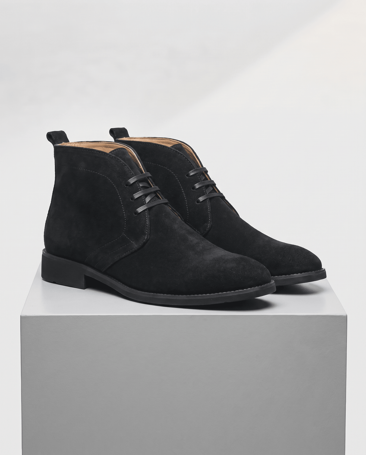 Pair of black suede lace-up chukka boots on a gray display block.