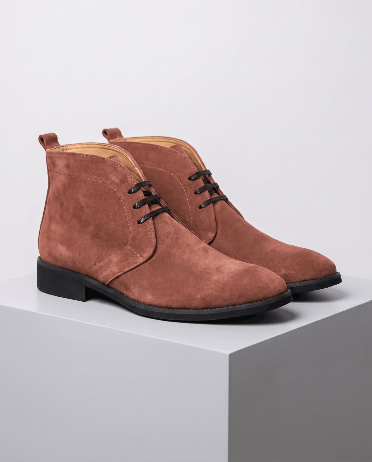 Pair of brown suede lace-up chukka boots on a gray display block.