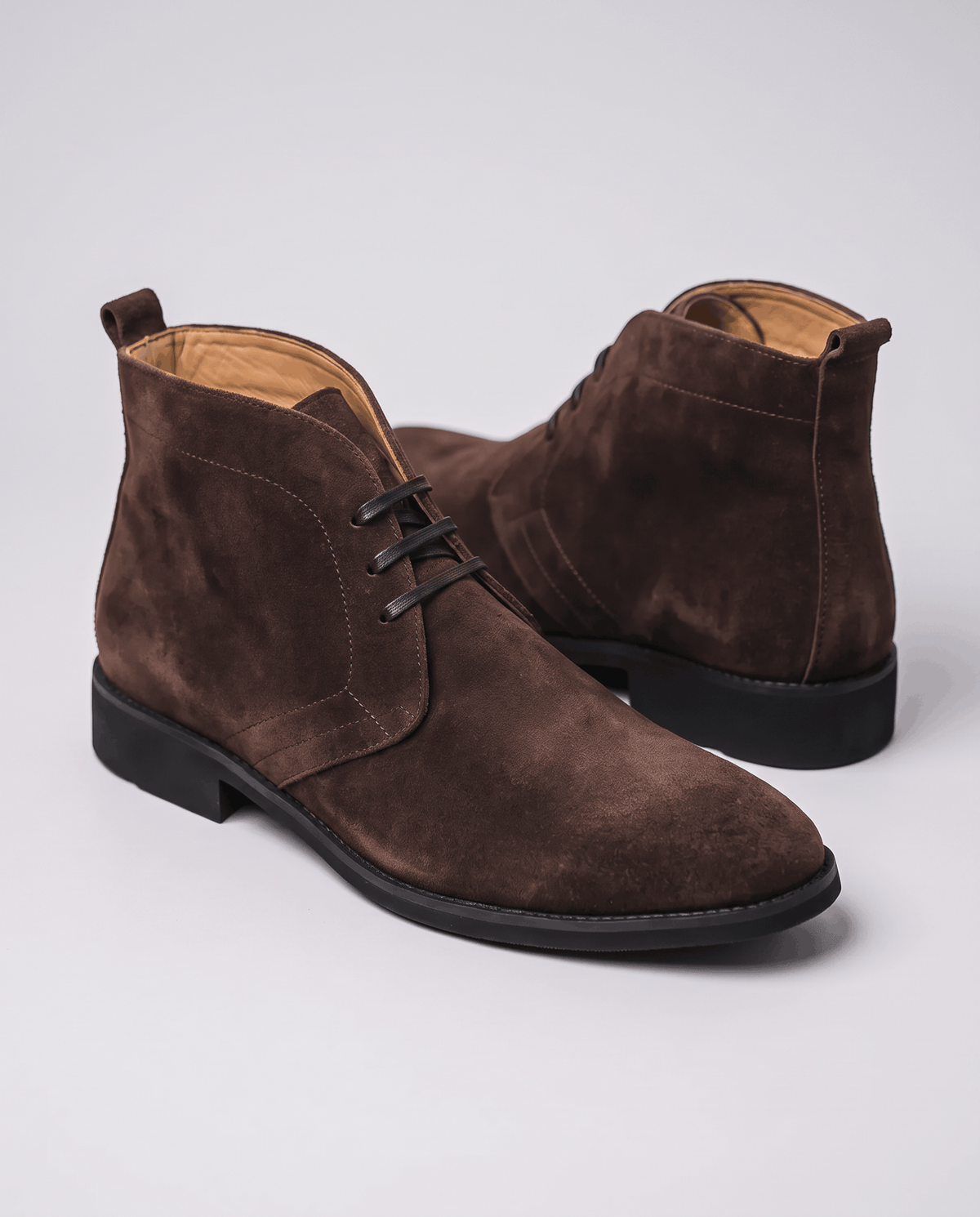 Dark brown suede chukka boots with a black sole shown at an angle.