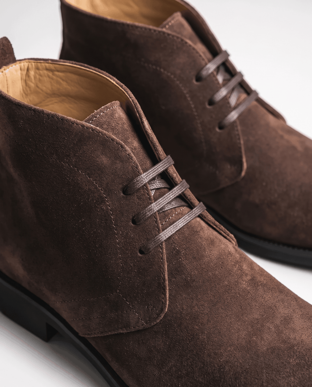 Close-up of dark brown suede chukka boot with short lace-up and tan lining.