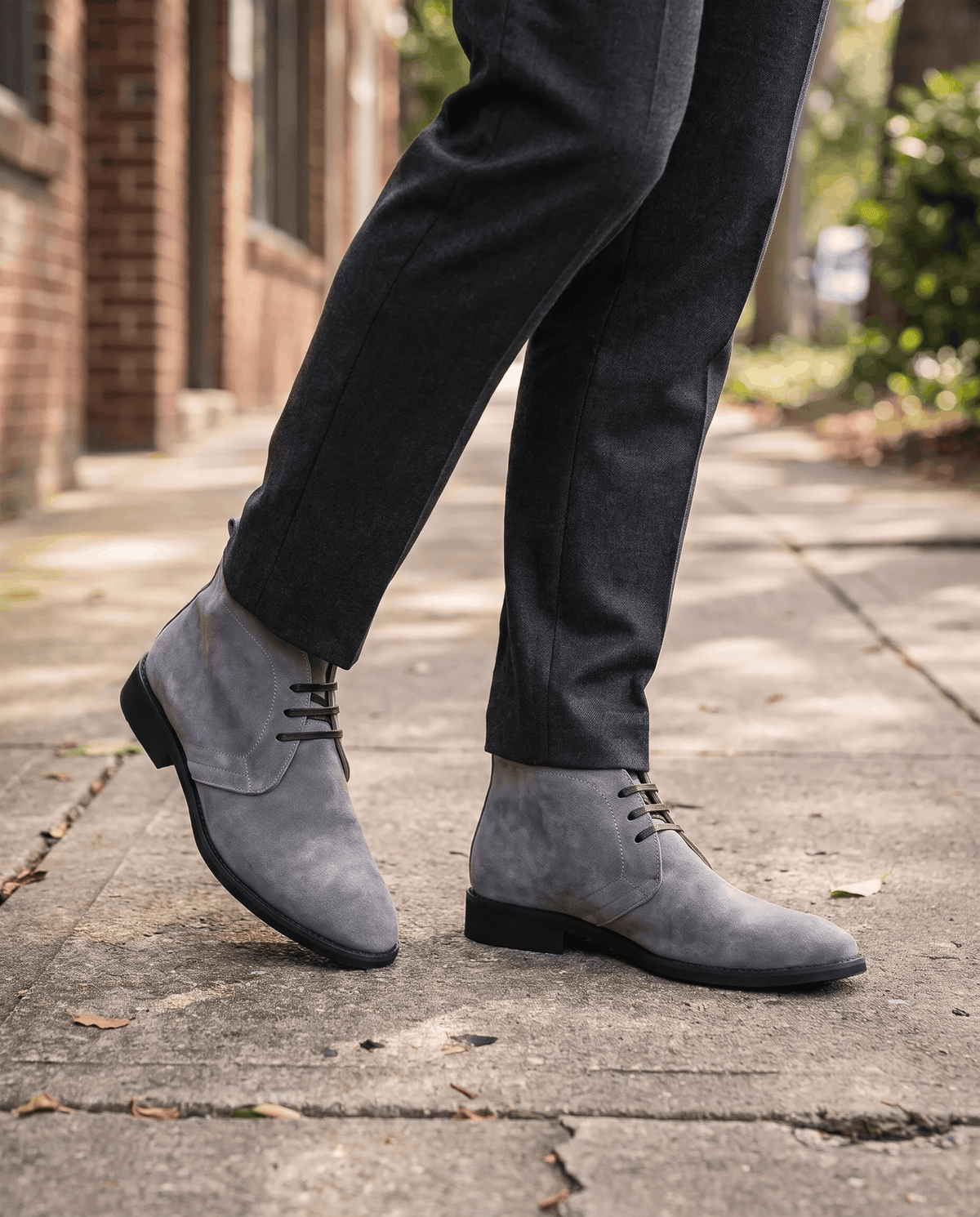Man walking in gray suede chukka boots with dark trousers on a pavement.