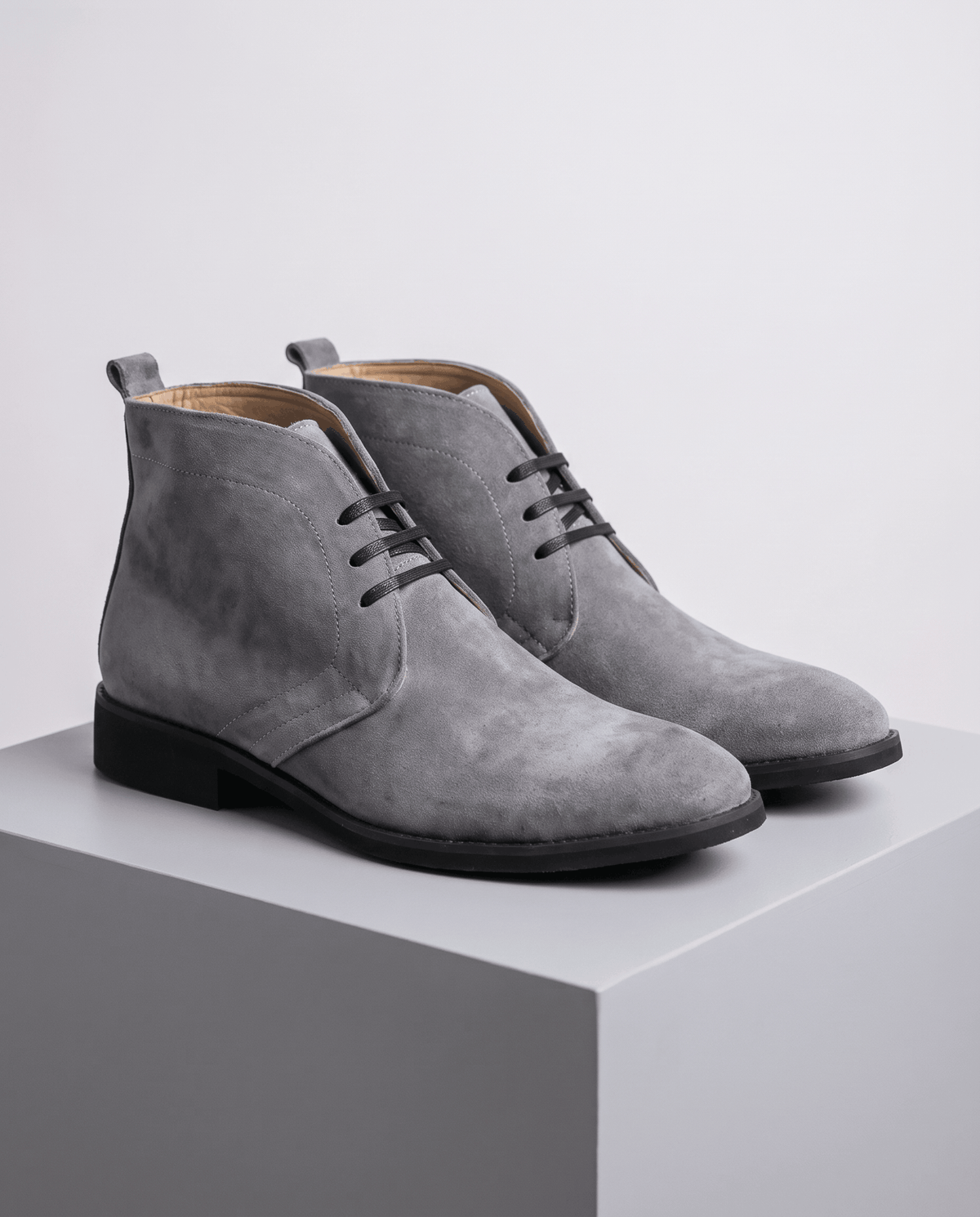 Pair of gray suede lace-up chukka boots on a gray display block.