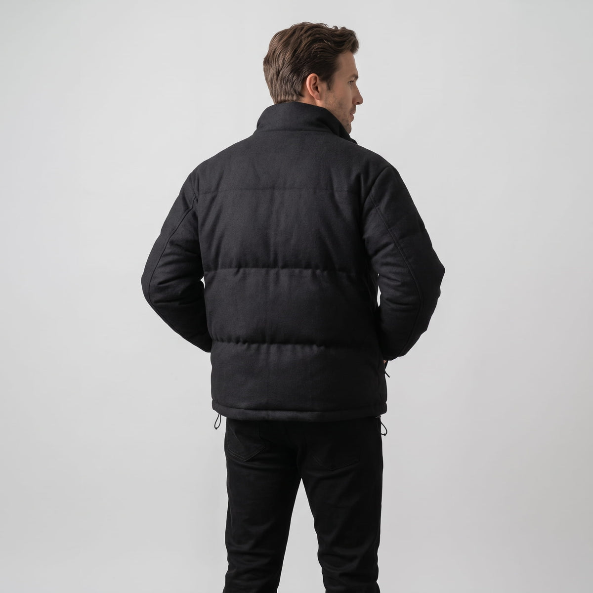 Back view in black showing the boxy quilted shape and drawcord at the hem