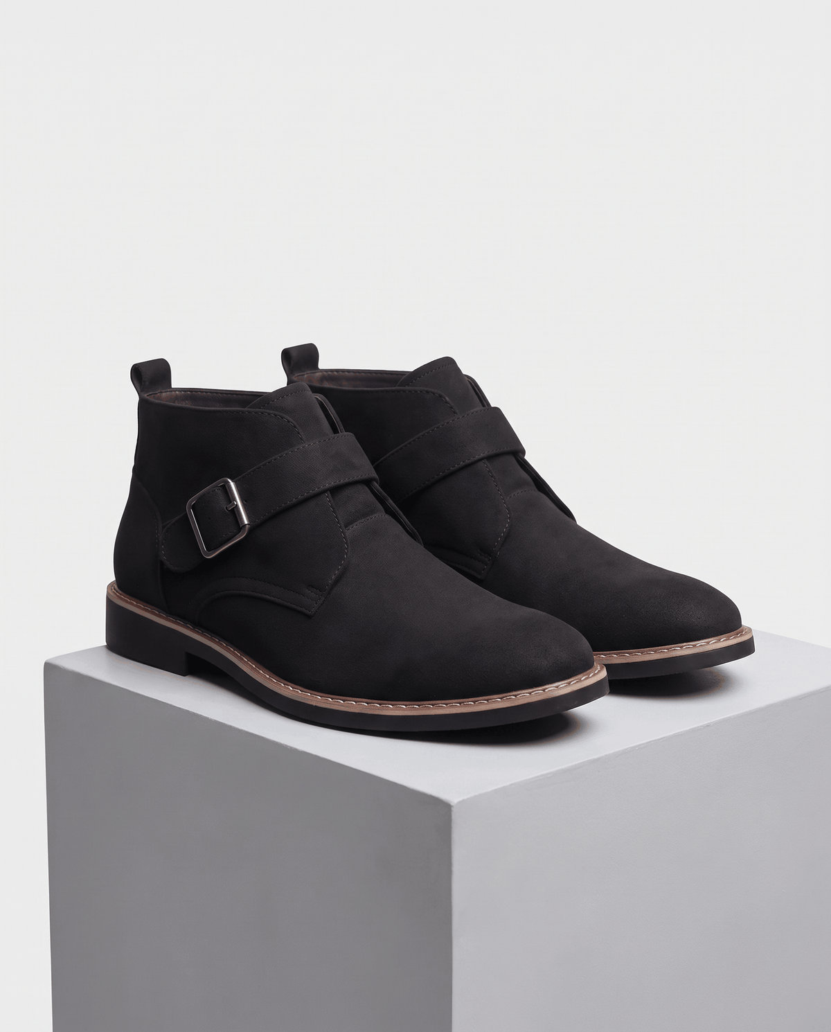 Pair of black suede boots with buckle straps on a grey stone pedestal