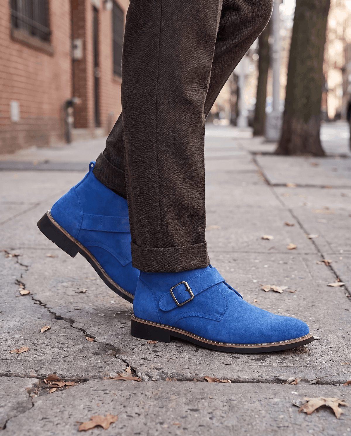 Blue suede boots worn with dark grey trousers on a brick sidewalk with fallen leaves