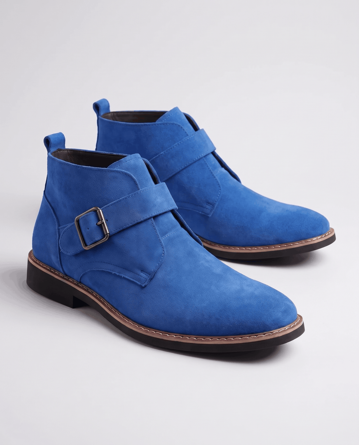 Pair of blue suede boots with buckle straps on a light grey studio backdrop