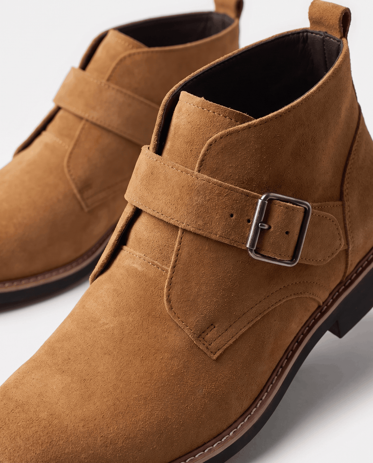 Close-up of the metal buckle and strap across the instep of a tan suede boot