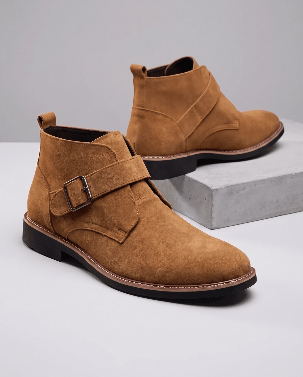 Tan suede boot with buckle strap in front, second boot resting on a grey block