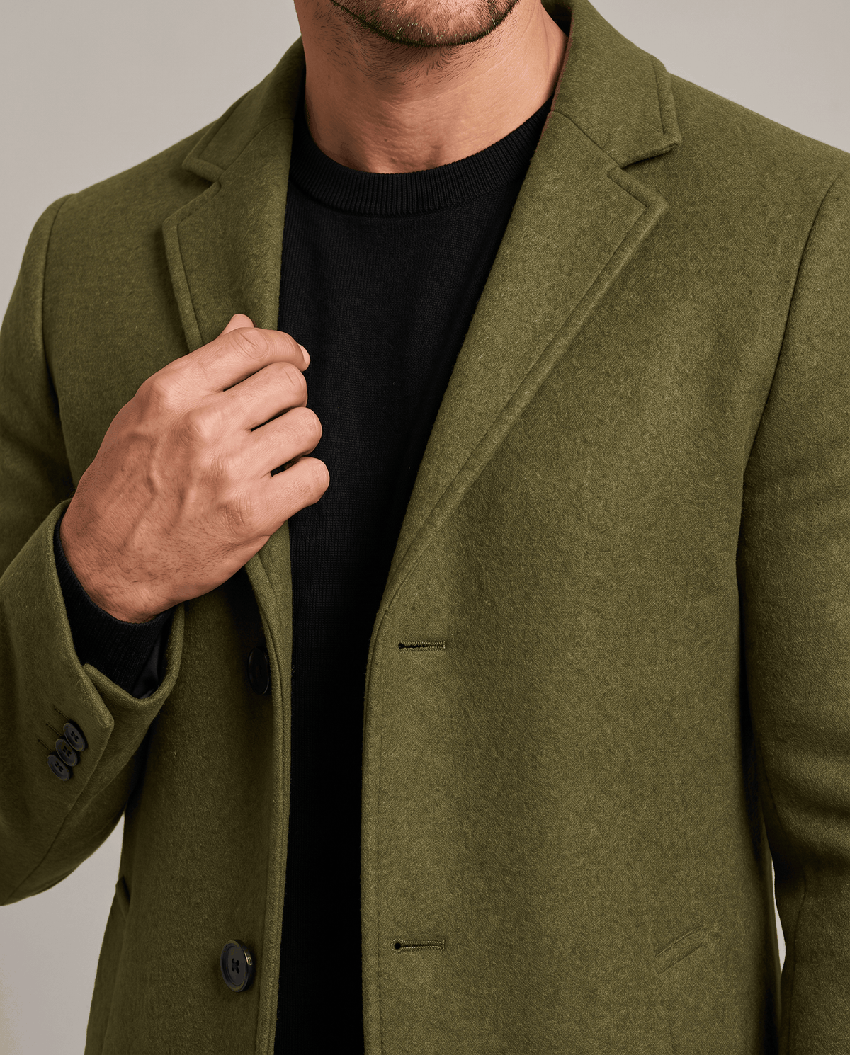 Close-up of the army green overcoat's notch lapel and button front with one hand at the chest
