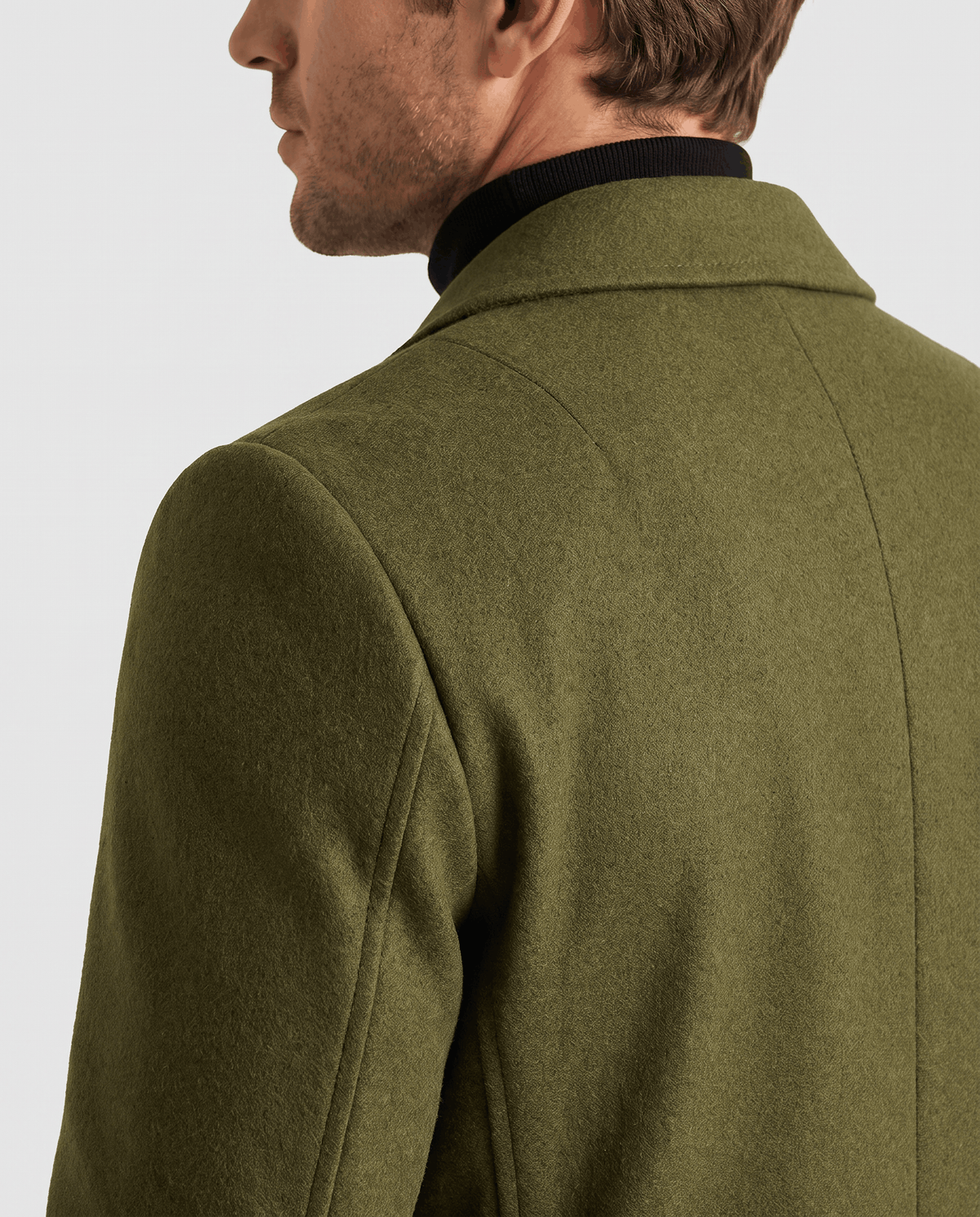 Side view of the army green overcoat's shoulder seam and collar, worn over a black turtleneck