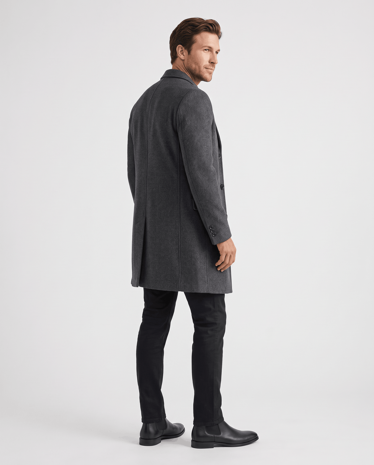 Three-quarter back view of the dark gray overcoat worn with black trousers and shoes