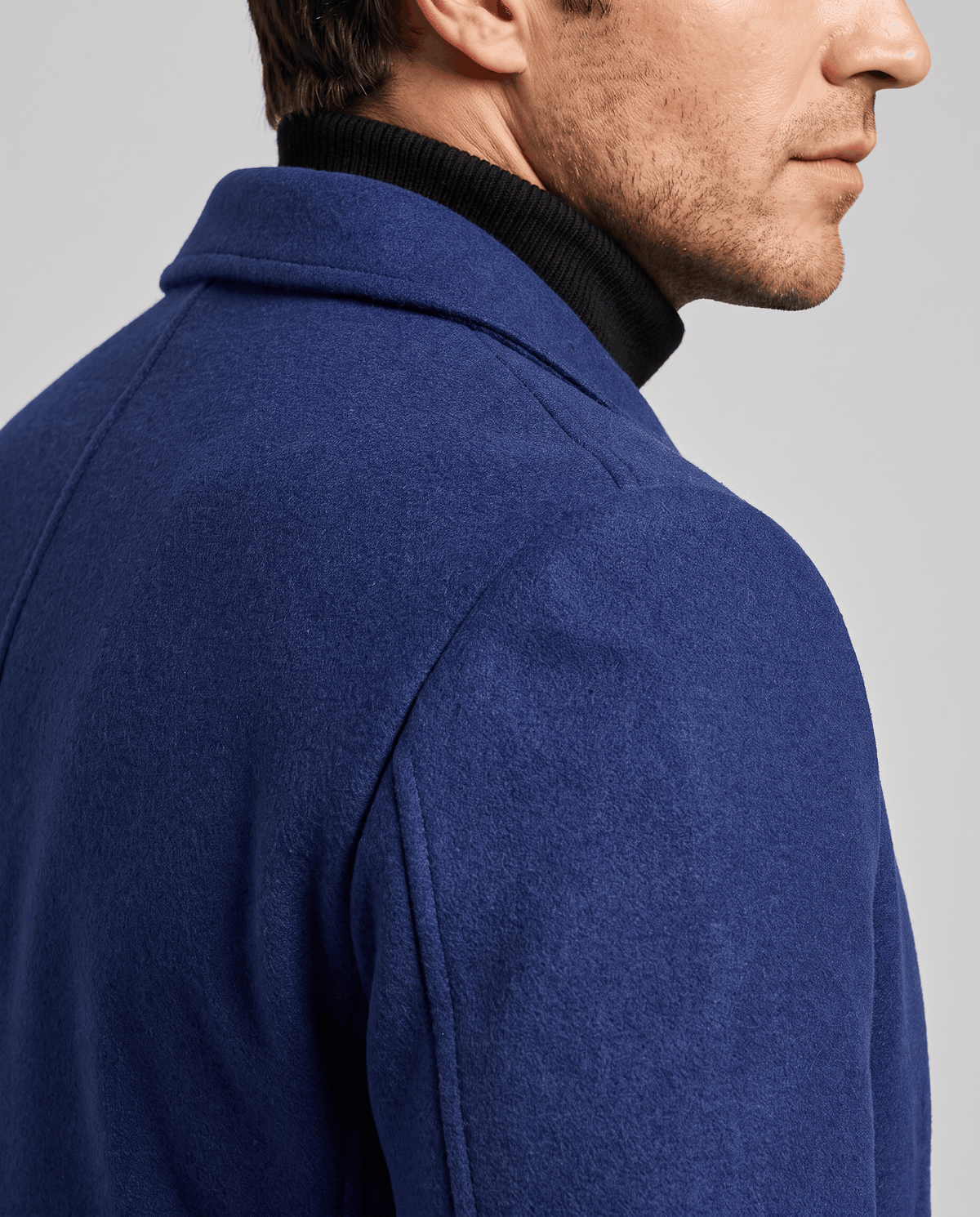 Close-up of the blue overcoat's collar and shoulder seam in a smooth, even fabric