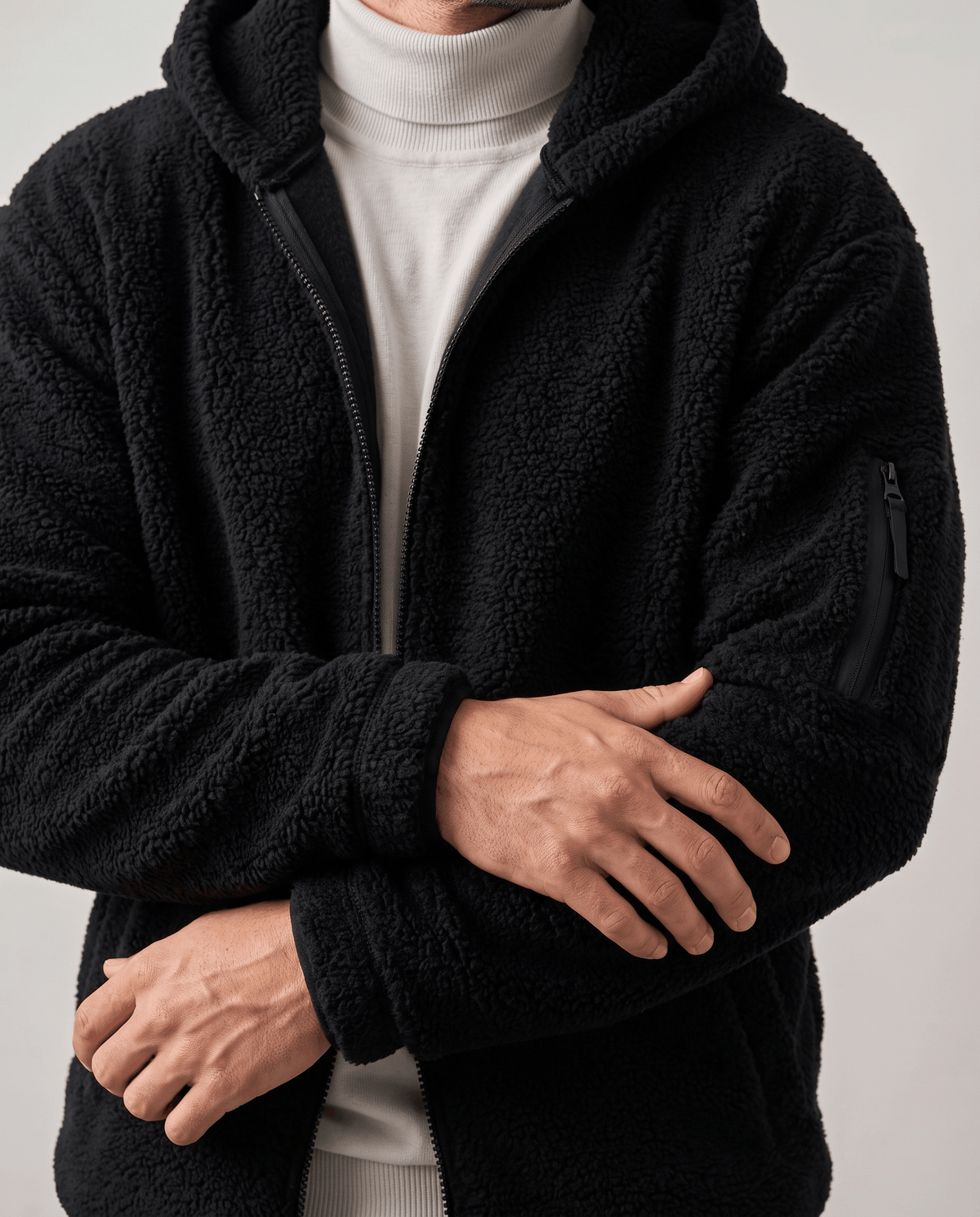 Arms crossed over cream turtleneck showing black sleeve zip pocket