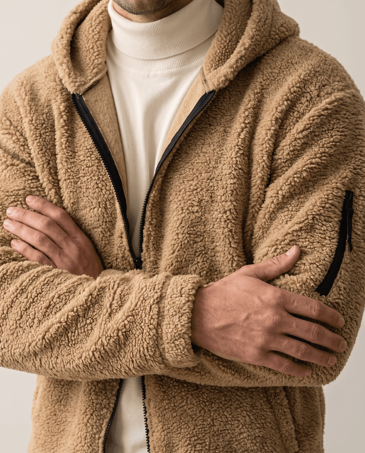 Arms crossed over cream turtleneck showing khaki zip sleeve pocket detail