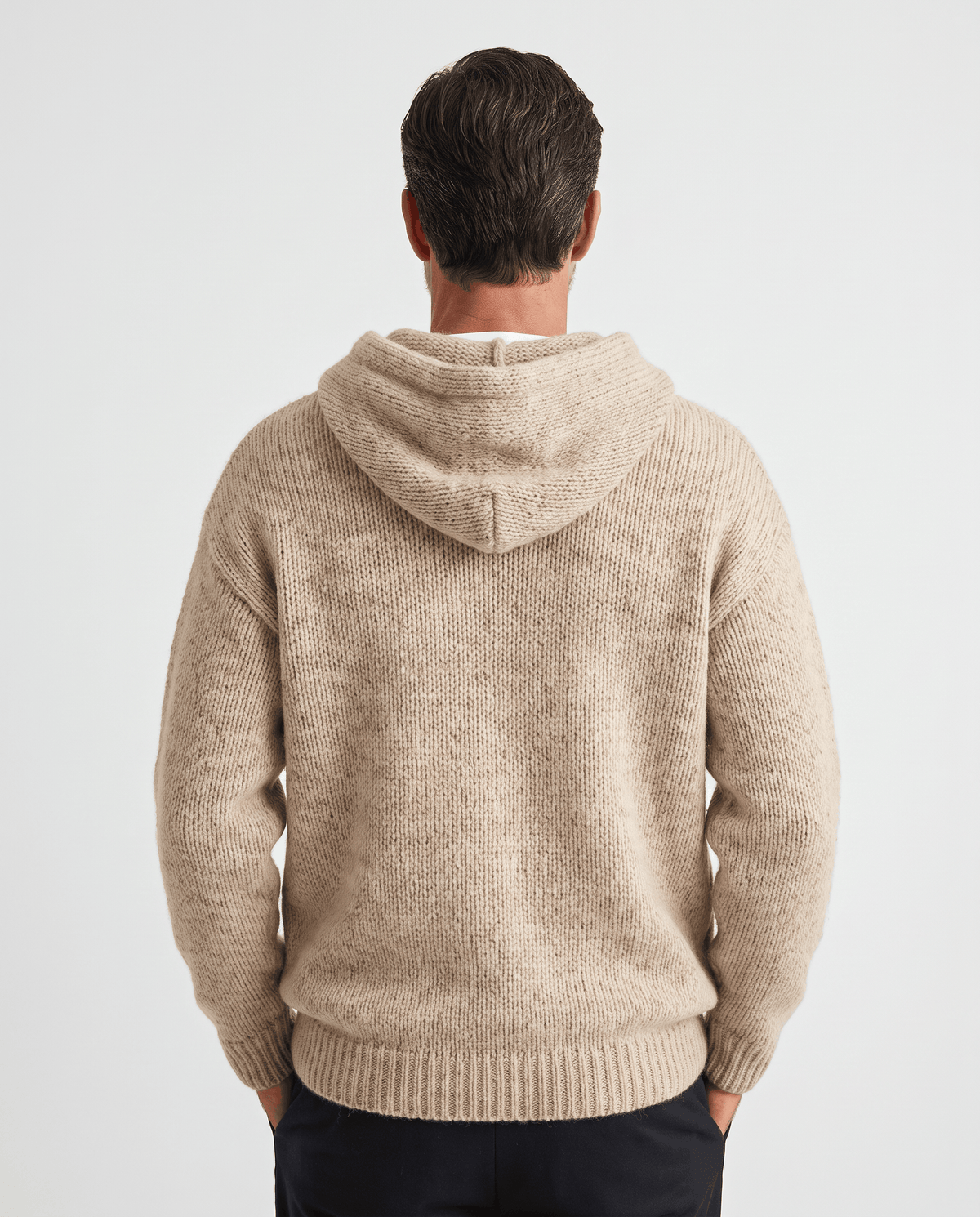 Back view of a beige knit pullover showing the hood resting between the shoulders