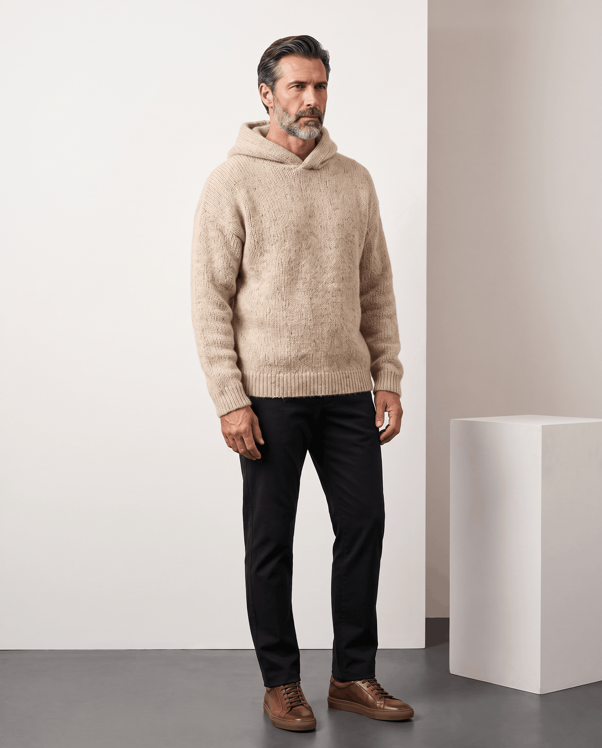 Full-length look: beige loose-fit knit sweater with a hood, black trousers and brown shoes