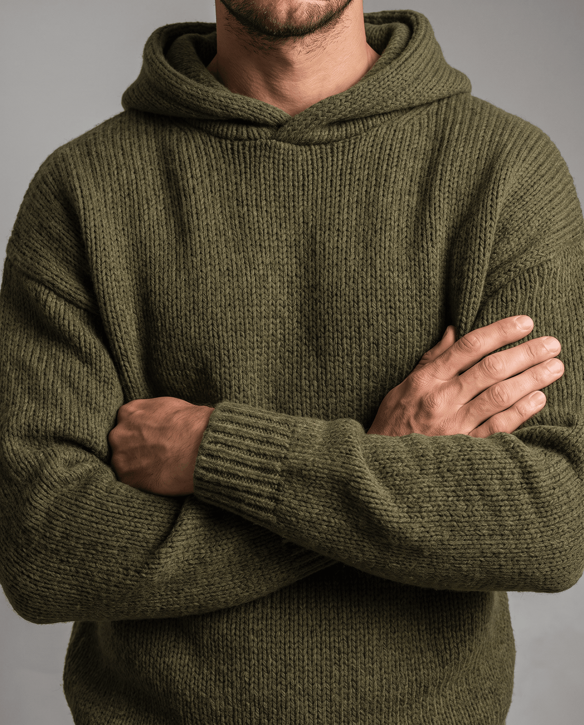 Close-up of a green textured knit sweater with arms crossed and ribbed cuffs showing