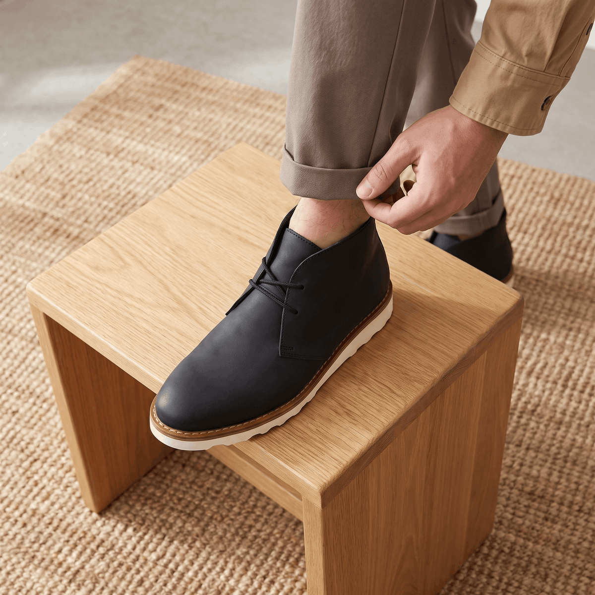 Person putting on a black two-eyelet chukka boot while seated.