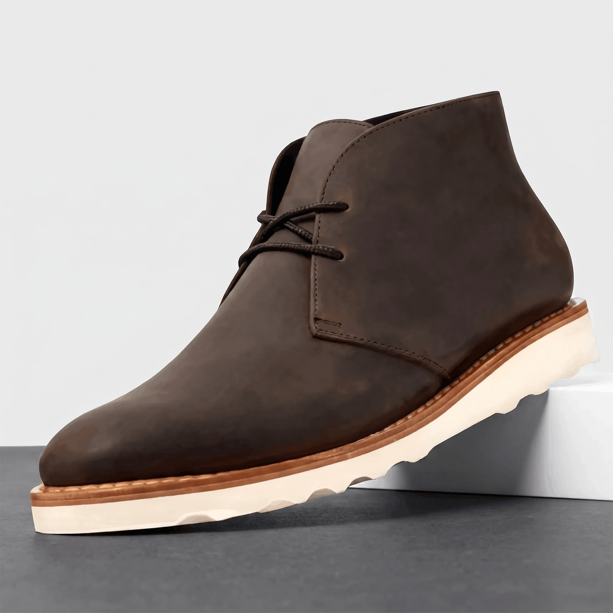 Dark brown matte chukka boot with a chunky scalloped outsole on a white pedestal.