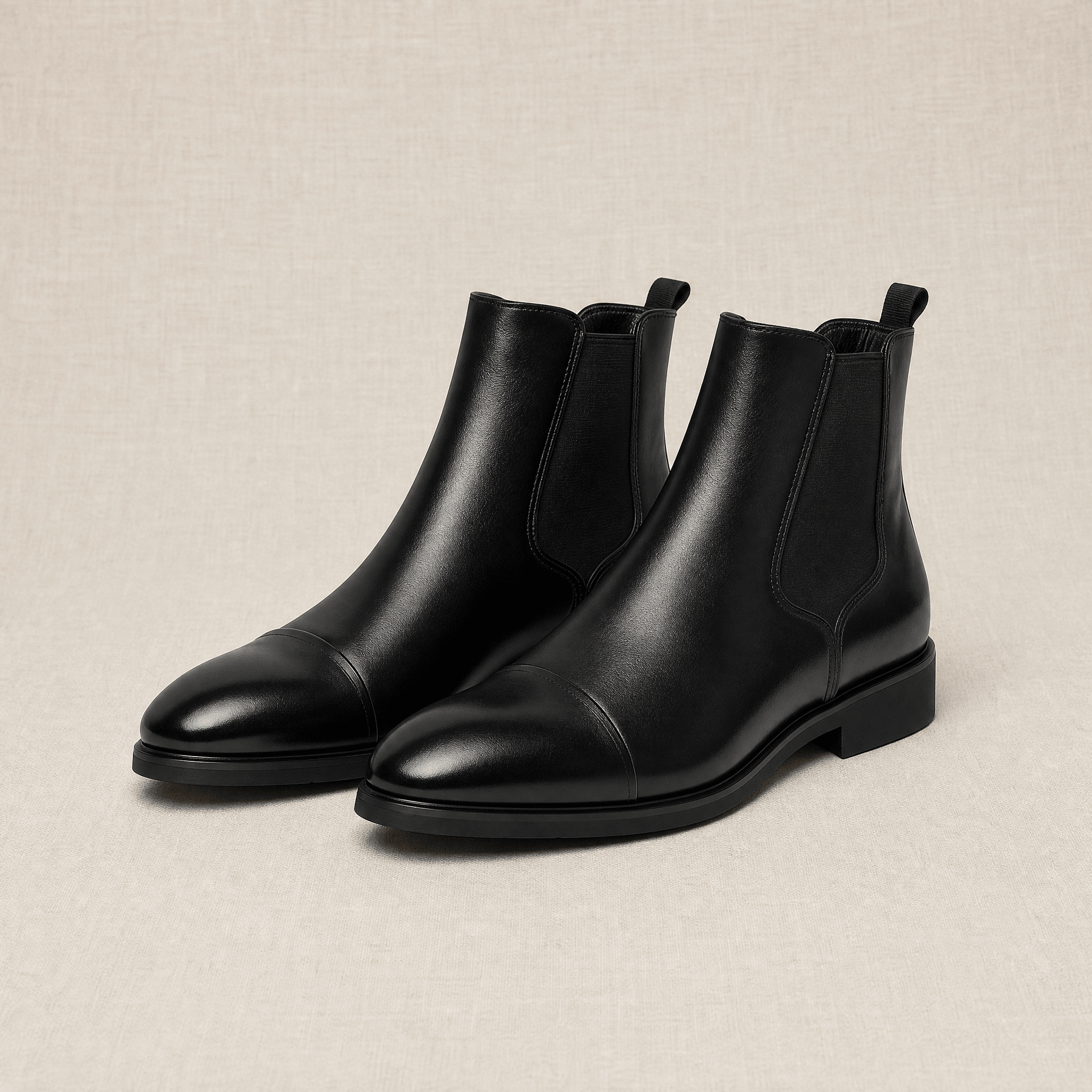 Black vegan leather cap toe Chelsea boots with elastic side gussets and a treaded rubber outsole on a neutral background.