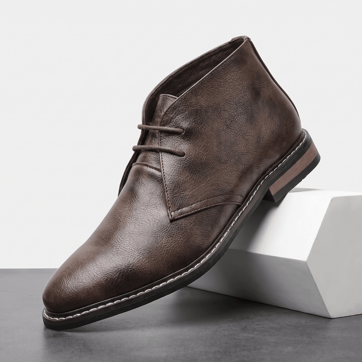 Brown vegan leather chukka boot with three-eyelet lacing, displayed on a white pedestal.