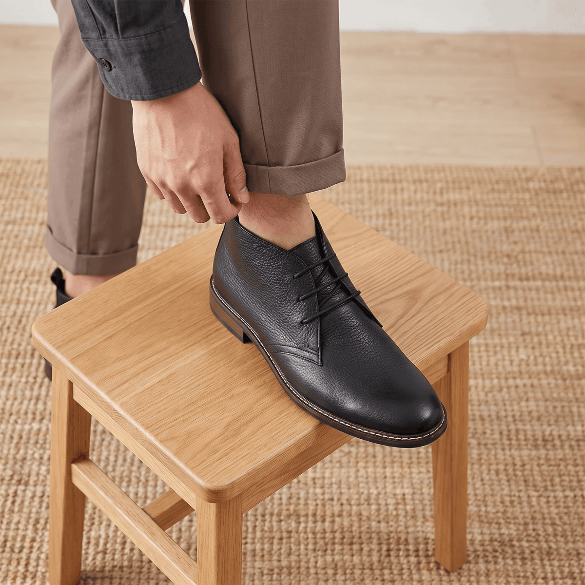 Black vegan leather chukka boots with lug soles worn with dark trousers indoors.
