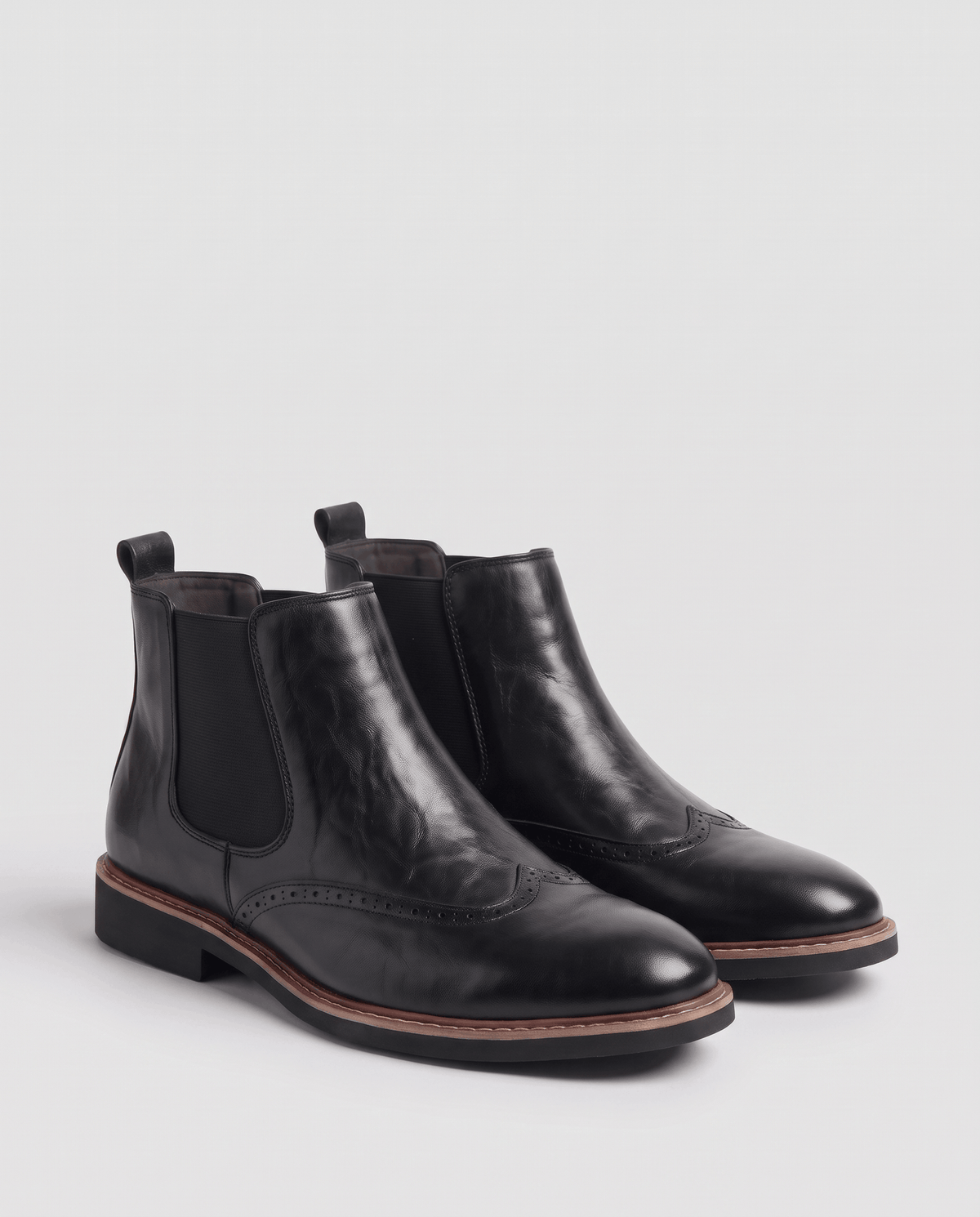 Pair of black brogue boots with elastic side panels on a grey studio backdrop