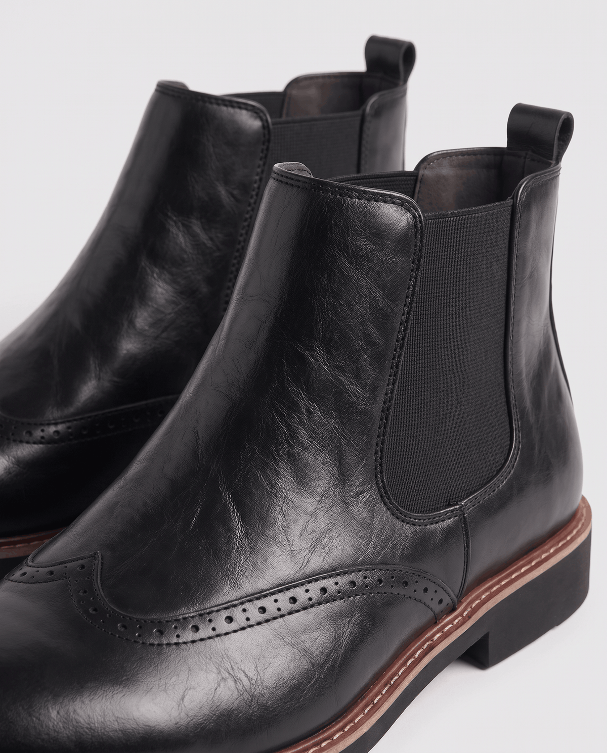 Close-up of black boots showing elastic side panels, pull tabs and brogue toe detailing