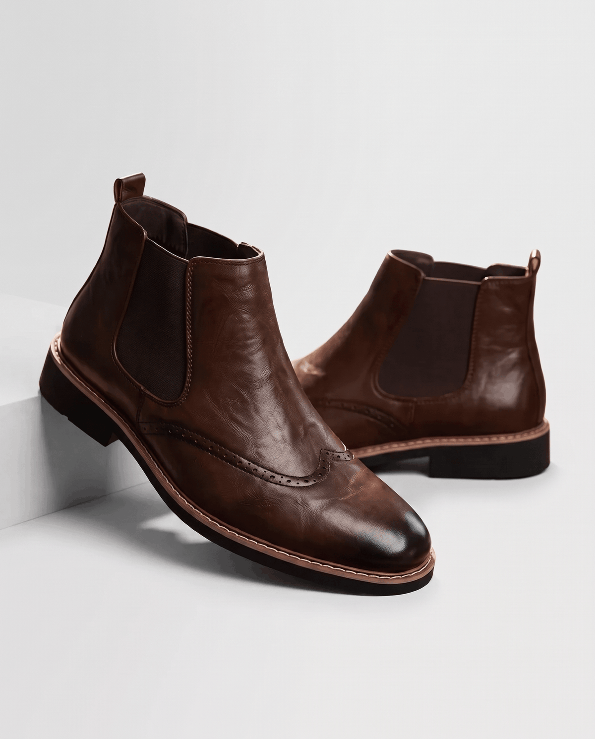 Brown brogue ankle boots with elastic side panels, angled pair showing dark sole and stitched edge