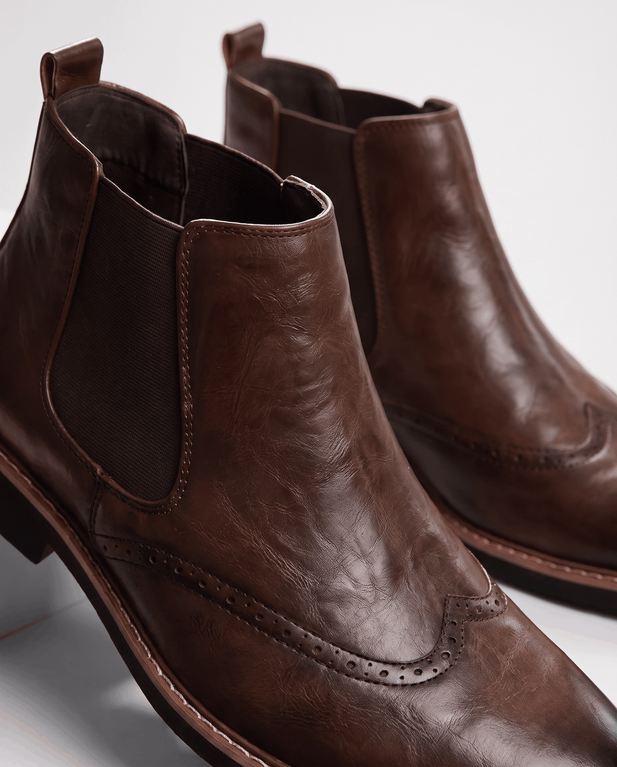 Close-up of wingtip brogue perforations and elastic side panel on a brown boot