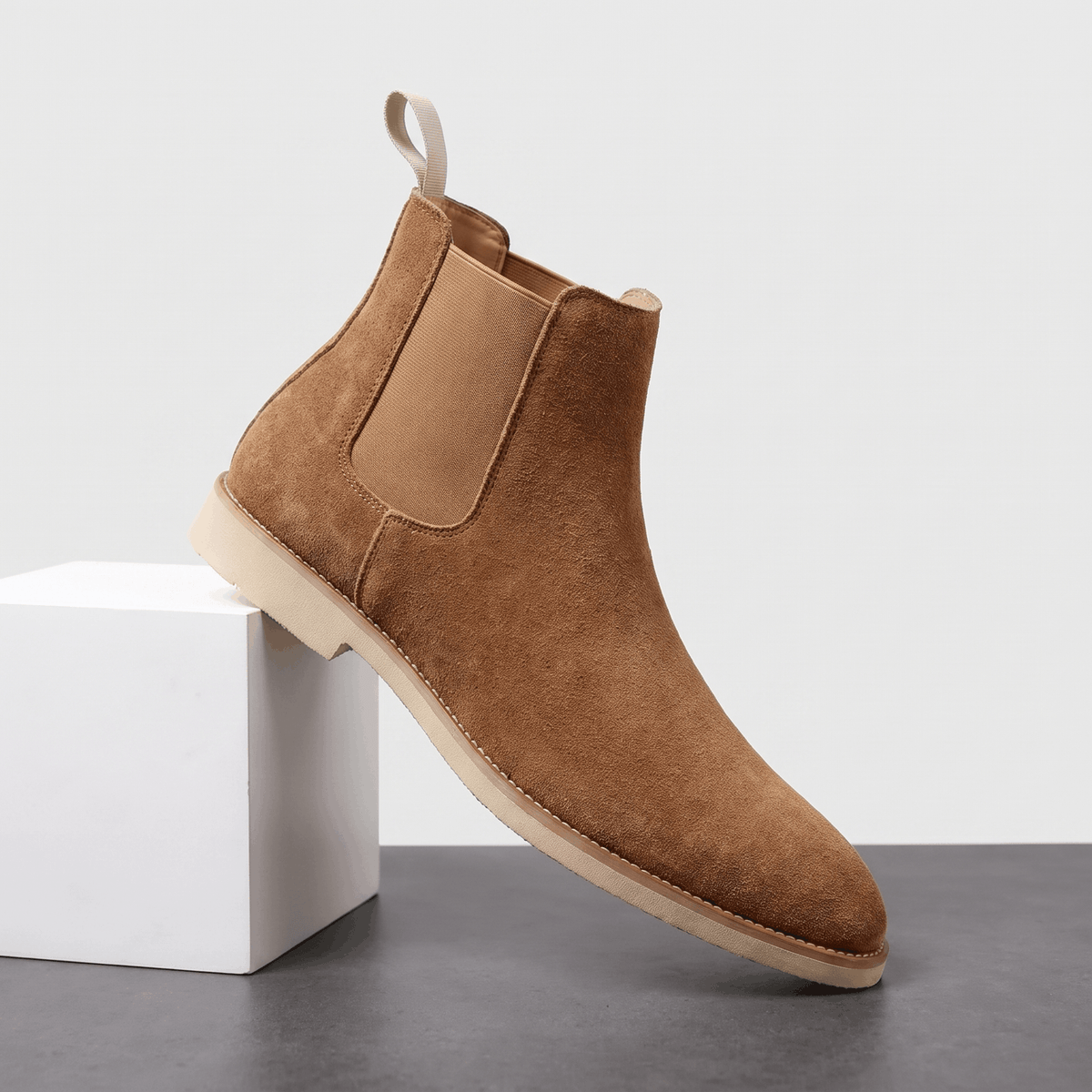Single camel vegan suede Chelsea boot with a high shaft and block heel, displayed on a white pedestal.