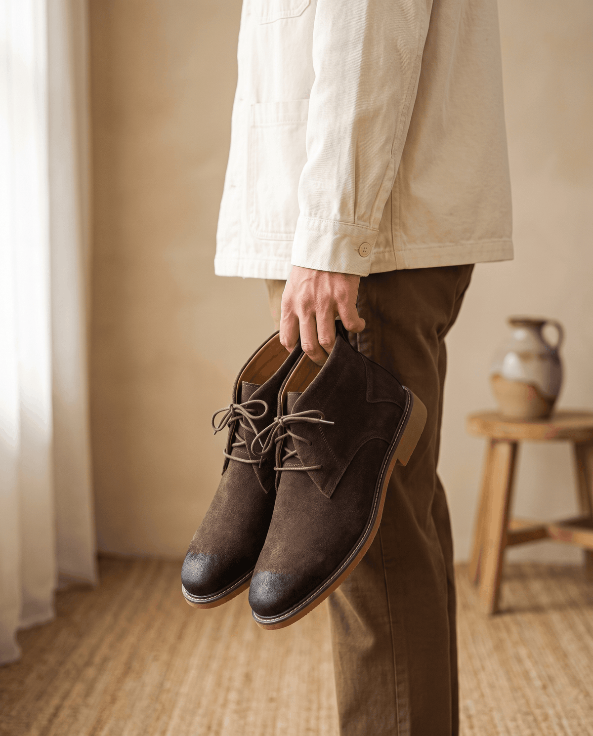Dark brown vegan suede chukka boots with three-eyelet lacing and a welted rubber outsole held by a person.