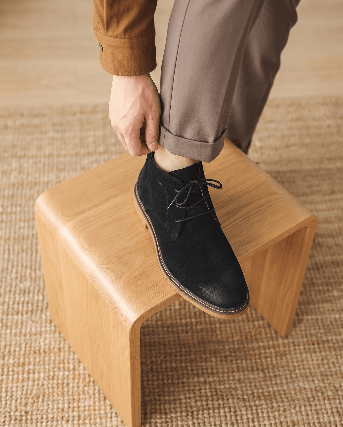 Black vegan suede chukka boots with three-eyelet lacing and a welted rubber outsole worn with cuffed trousers.