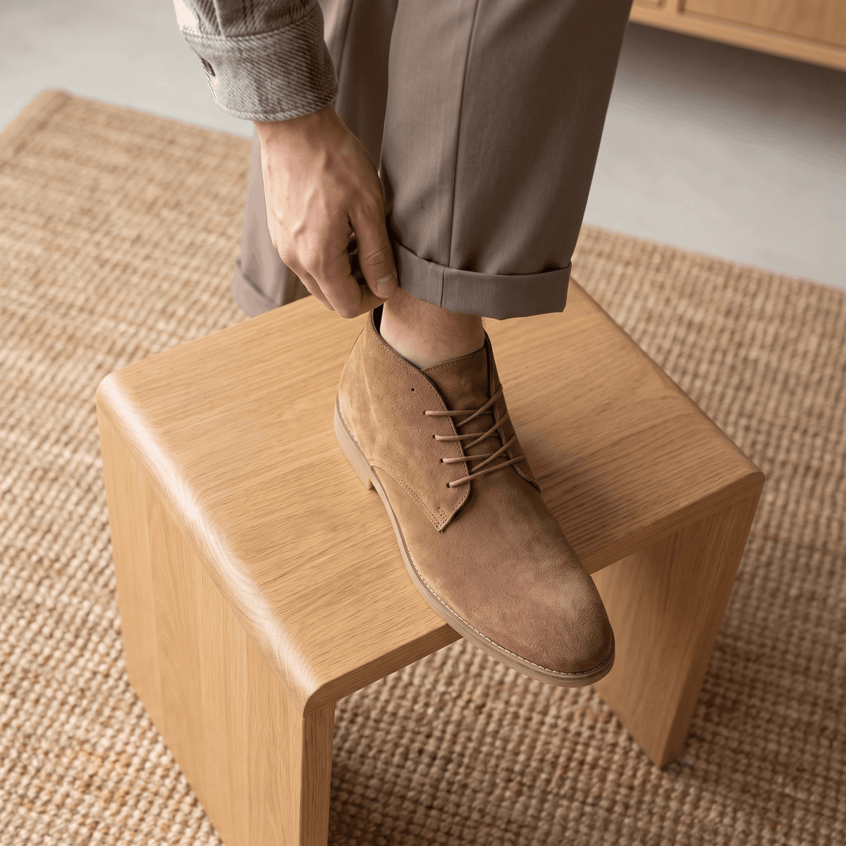Khaki vegan suede desert boot being worn while seated on a wooden stool.