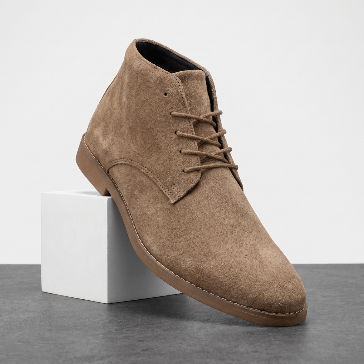 Brown vegan suede desert boot with a slim stitched sole, displayed on a white pedestal.