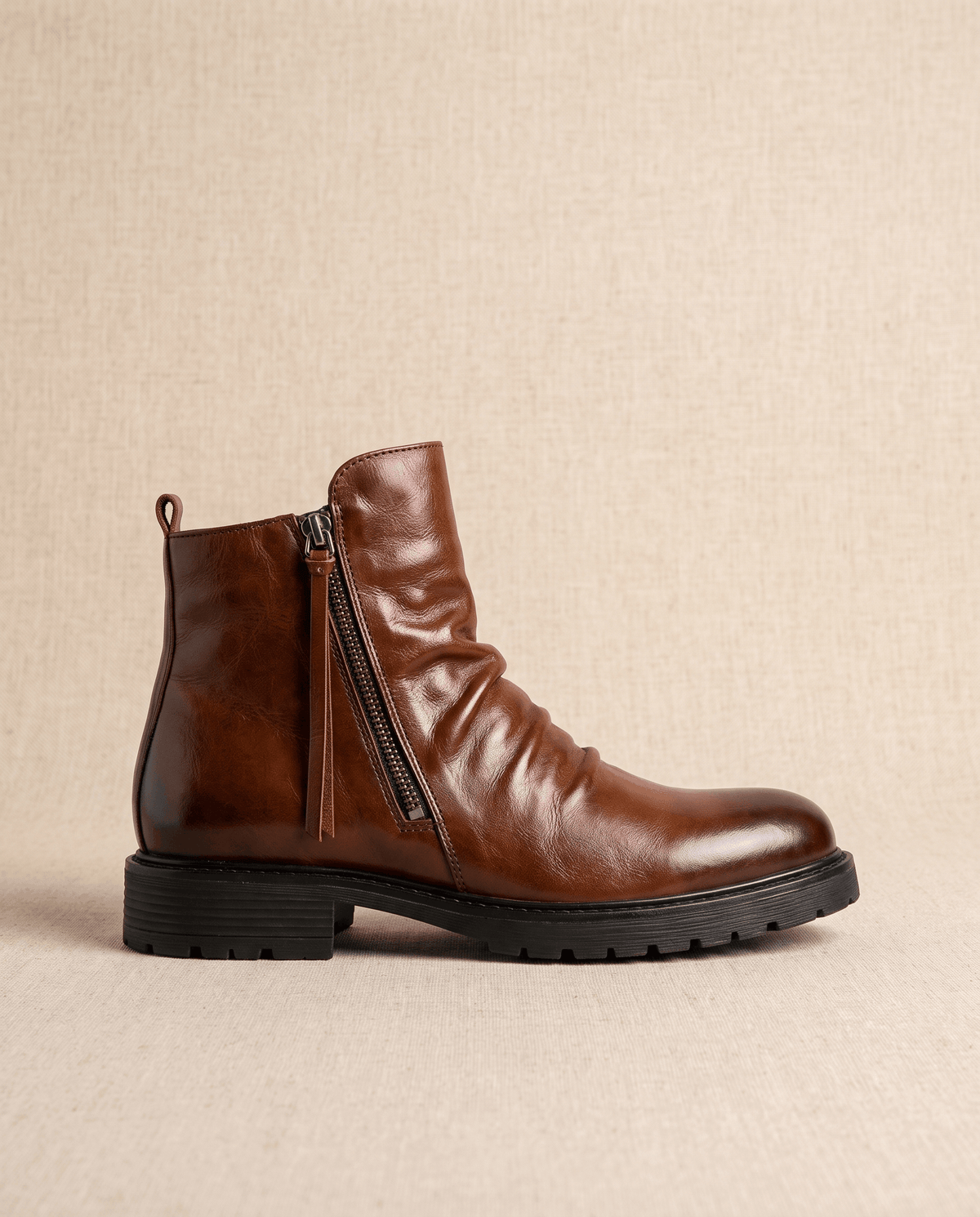 Brown waxed leather ankle boot with a ruched shaft, side zipper, and a black lugged rubber outsole.