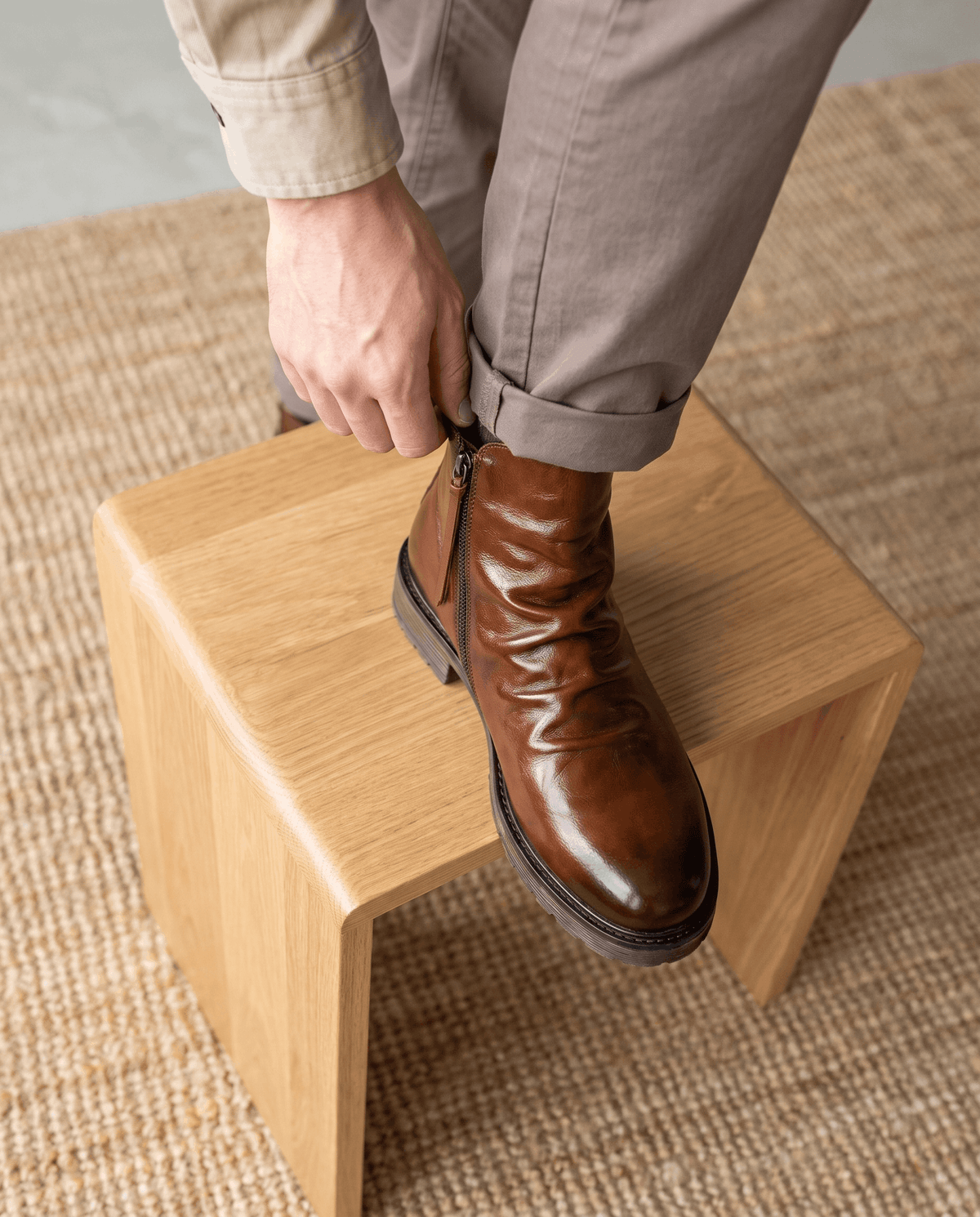 Brown waxed leather ankle boots with a ruched shaft and side zip, resting on a wooden stool.