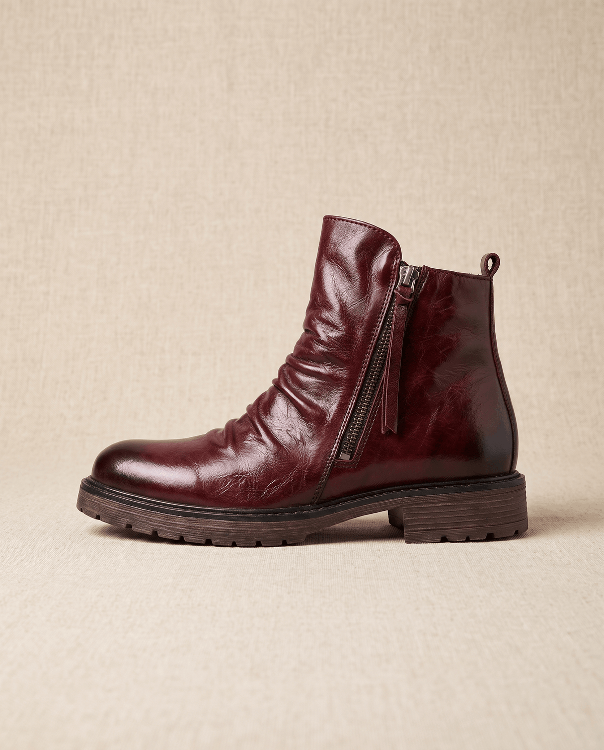 Dark red waxed leather ankle boot with a ruched shaft, side zip closure, and a rugged, slip-resistant rubber sole.