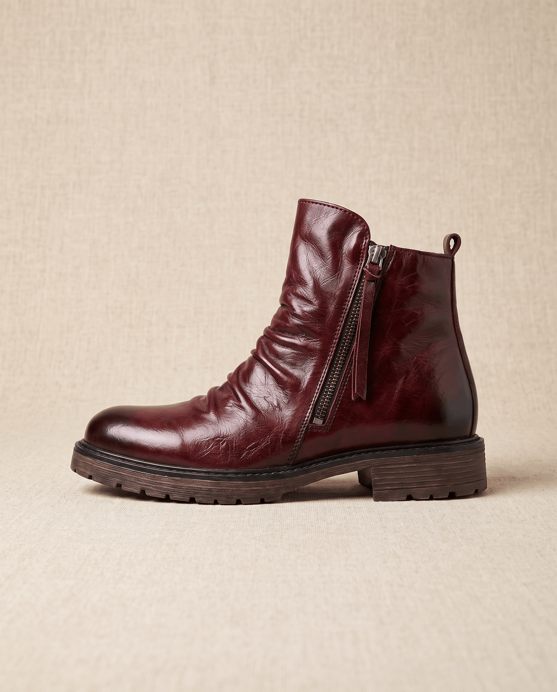 Dark red waxed leather ankle boot with a ruched shaft, side zip closure, and a rugged, slip-resistant rubber sole.